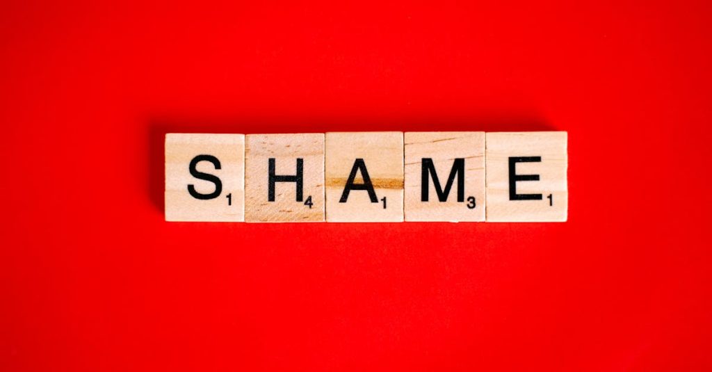 Scrabble tiles spelling the word 'Shame' on a vibrant red backdrop. Build shame resilience